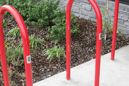 Red, commercial-grade inverted U bike racks installed outdoors in a landscaped area